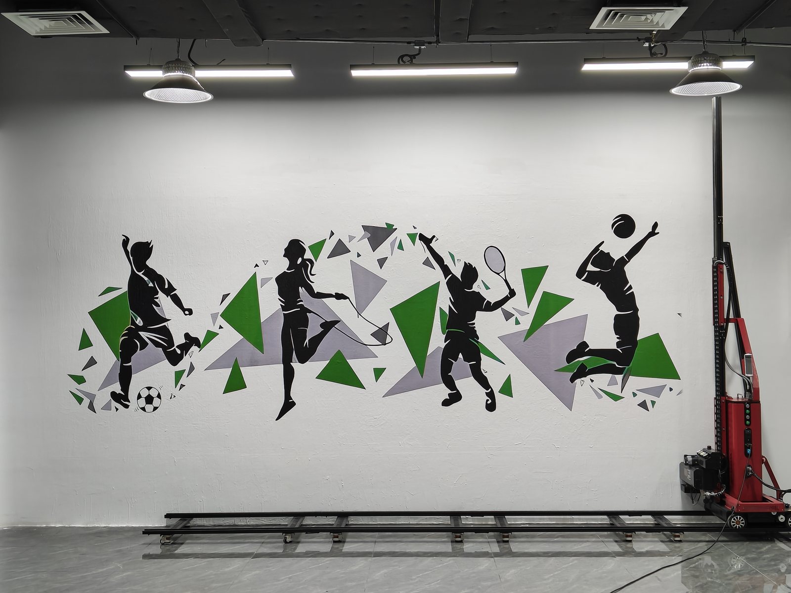 Silhouetted footballer, tennis player and basketball players printed across a wall in green and grey
